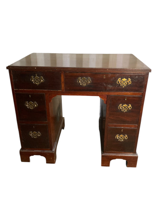 A George III crossbanded mahogany kneehole desk of six drawers with gilt handles