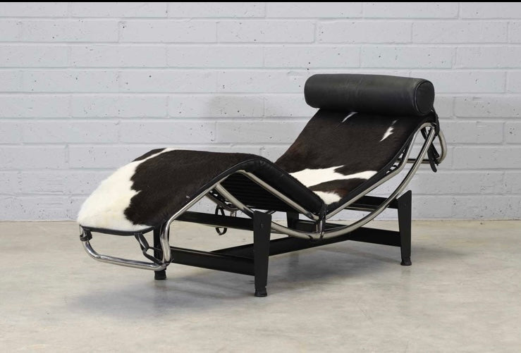 An 'LC4'  Le Corbusier Style chaise longue,upholstered in pony hide and with a black leather neck roll cushion to the chromium-plated tubular frame,