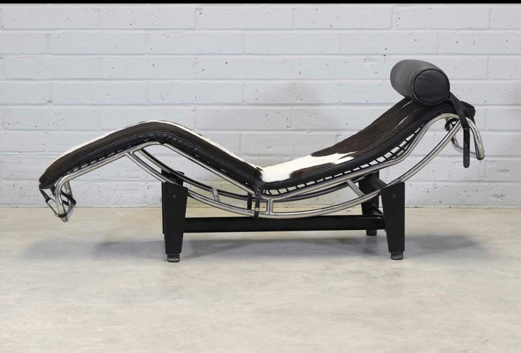 An 'LC4'  Le Corbusier Style chaise longue,upholstered in pony hide and with a black leather neck roll cushion to the chromium-plated tubular frame,